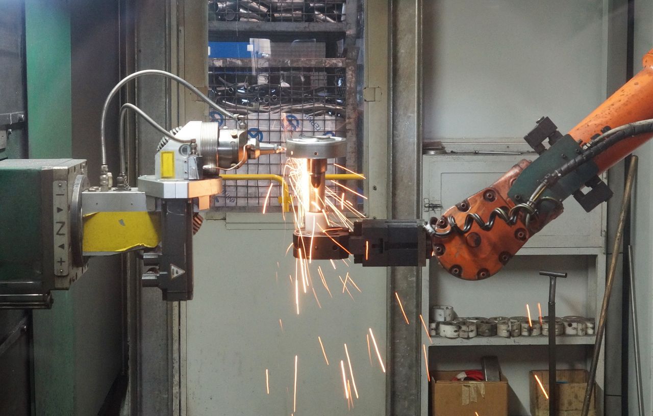 Services A robotic arm welding in an industrial setting, emitting bright sparks.
